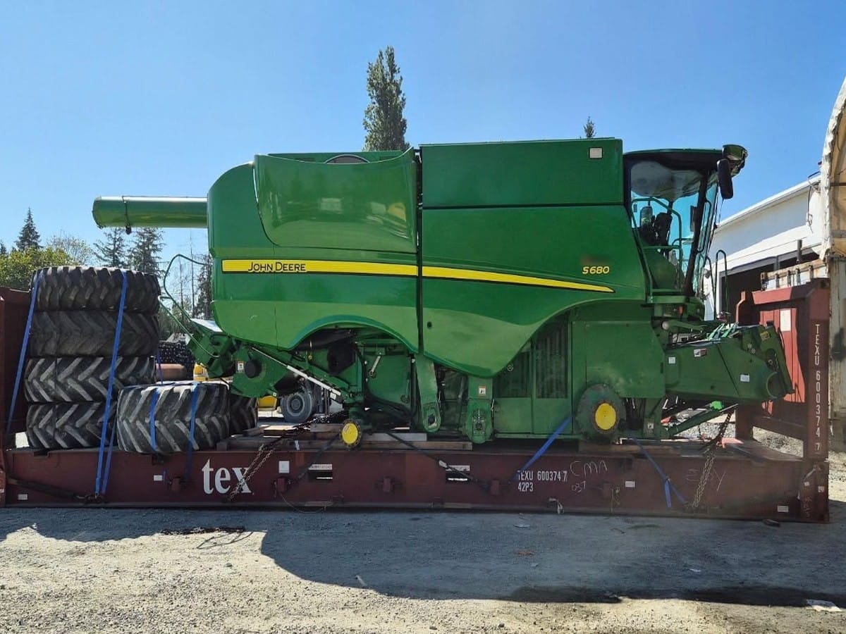 John Deere S680 combine strapped down on a Flat Rack with large tires stacked beside it