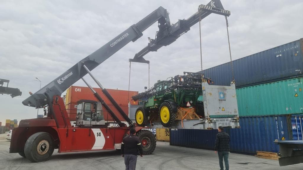 Port crane lifting a sprayer with customs and NCB certificates in hand