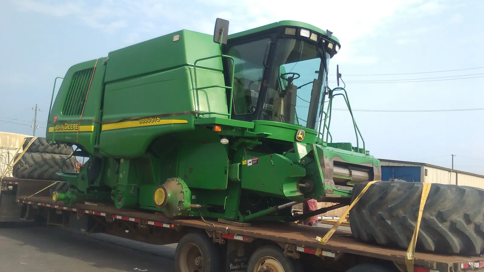 John Deere combine on a flatbed trailer with a large tire strapped beside it