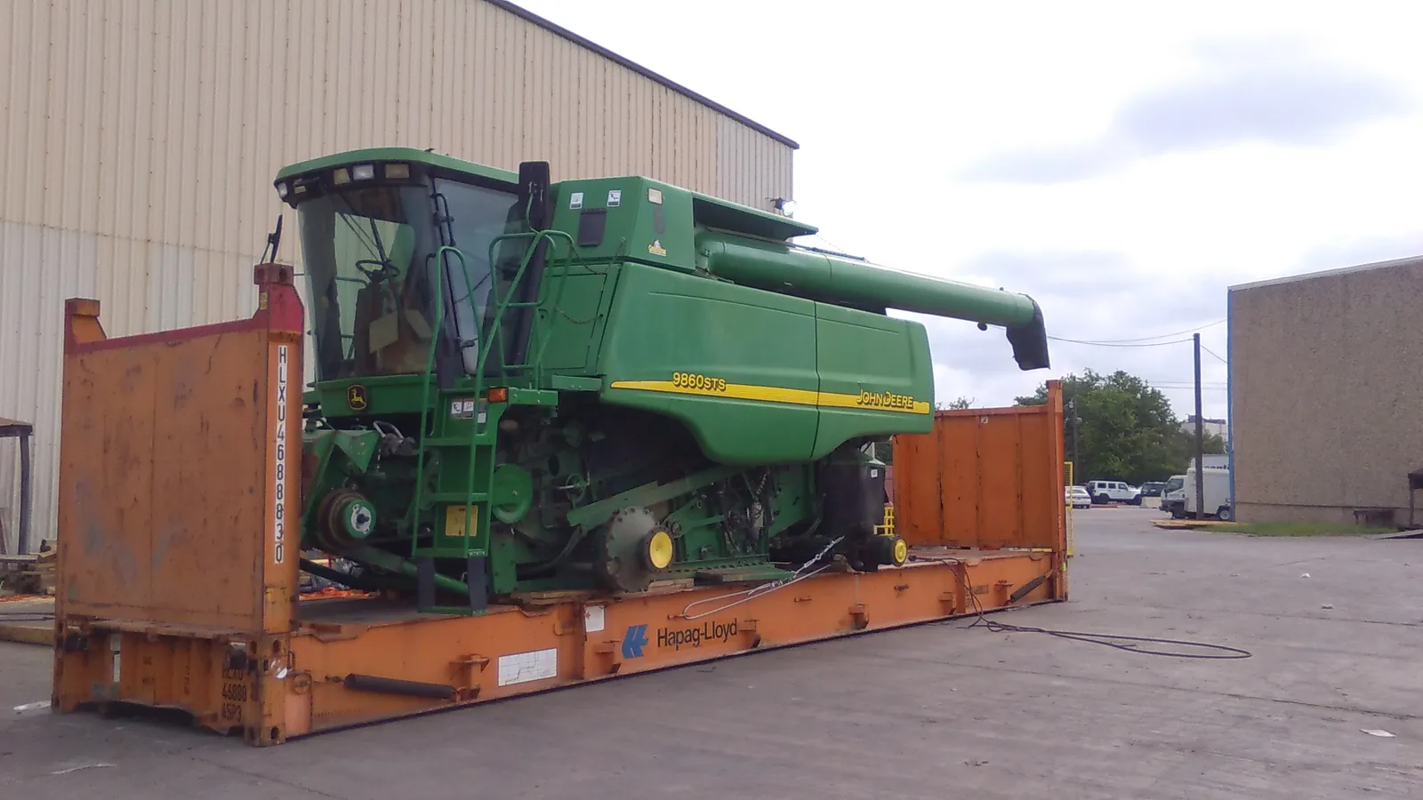 Комбайн John Deere 9860 STS зелёного цвета на оранжевой платформе Flat Rack на фоне стены склада