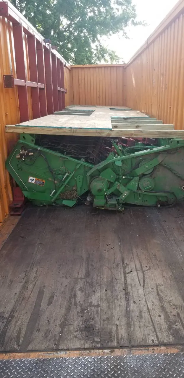 A green header lying in an open-top container with a wooden deck laid over it