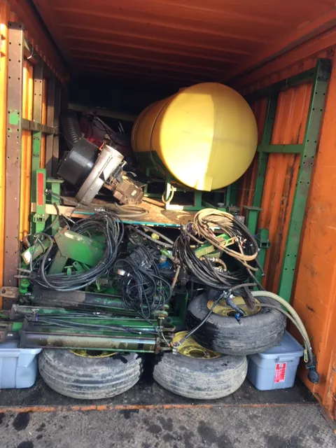 Container interior packed with hoses, tires, green machine frames and a yellow tank