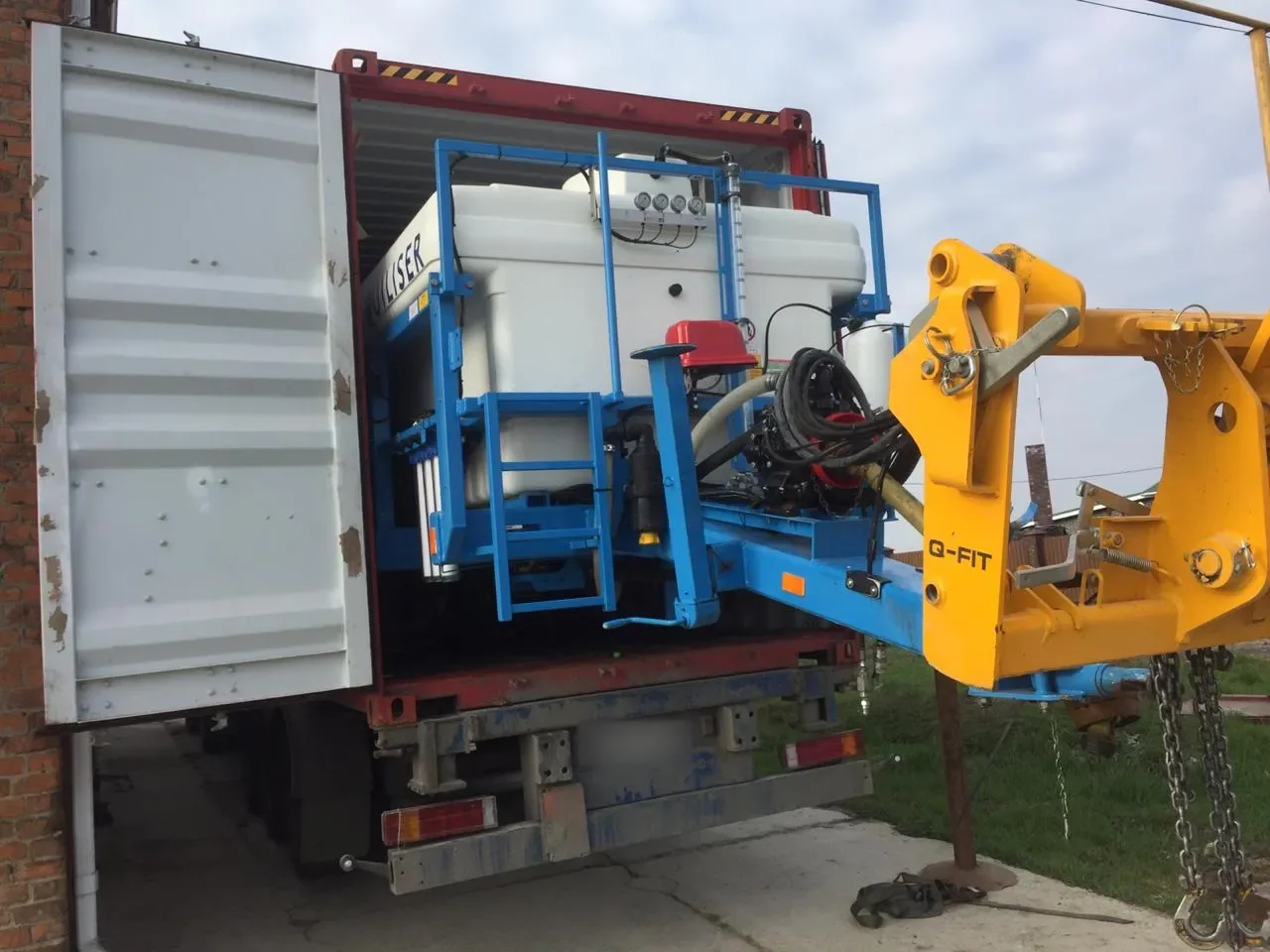 Liquid fertilizer equipment with a white tank at the open end of a container on a truck