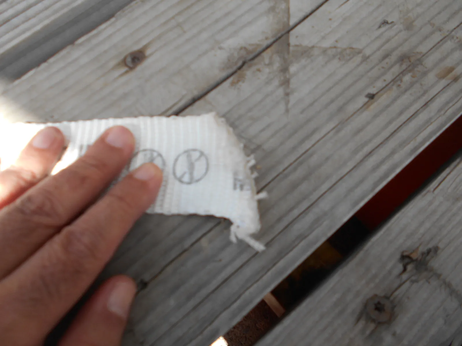 Hand holding a torn piece of white lashing strap with printed pictograms over a wooden deck