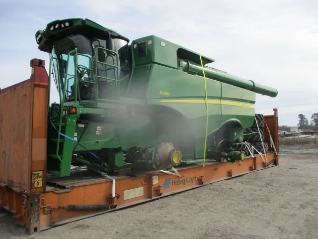 John Deere S680 combine strapped onto a flat rack, with large wheels stowed at the far end
