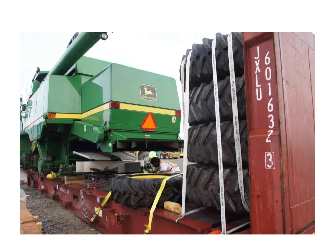 Комбайн John Deere на платформе flat rack, рядом стоят и закреплены крупные шины, у основания машины присел рабочий