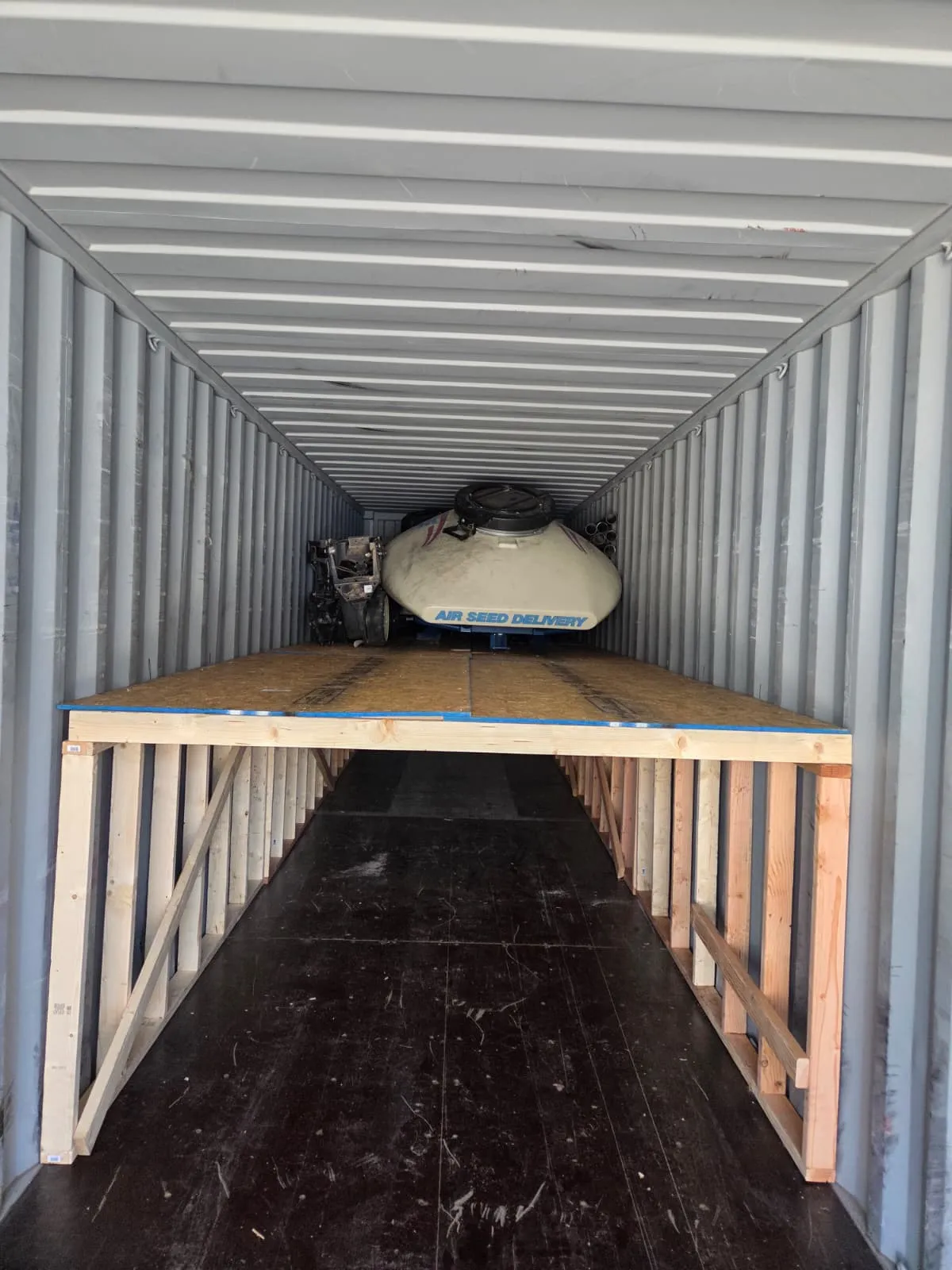 Inside a shipping container, a timber-framed wooden platform carries a large white tank at the far end