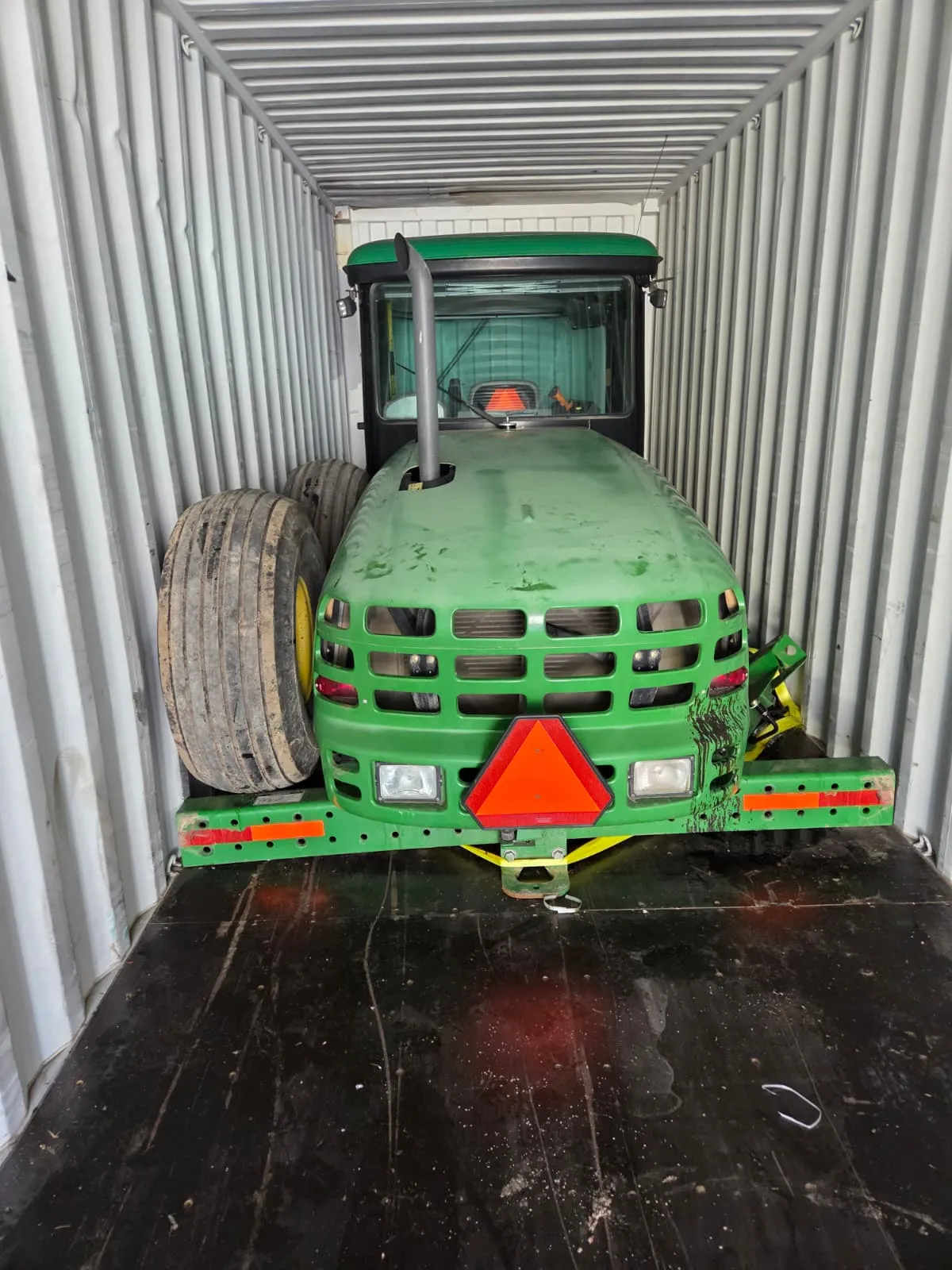 John Deere machine standing inside a shipping container with detached wheels beside its cab