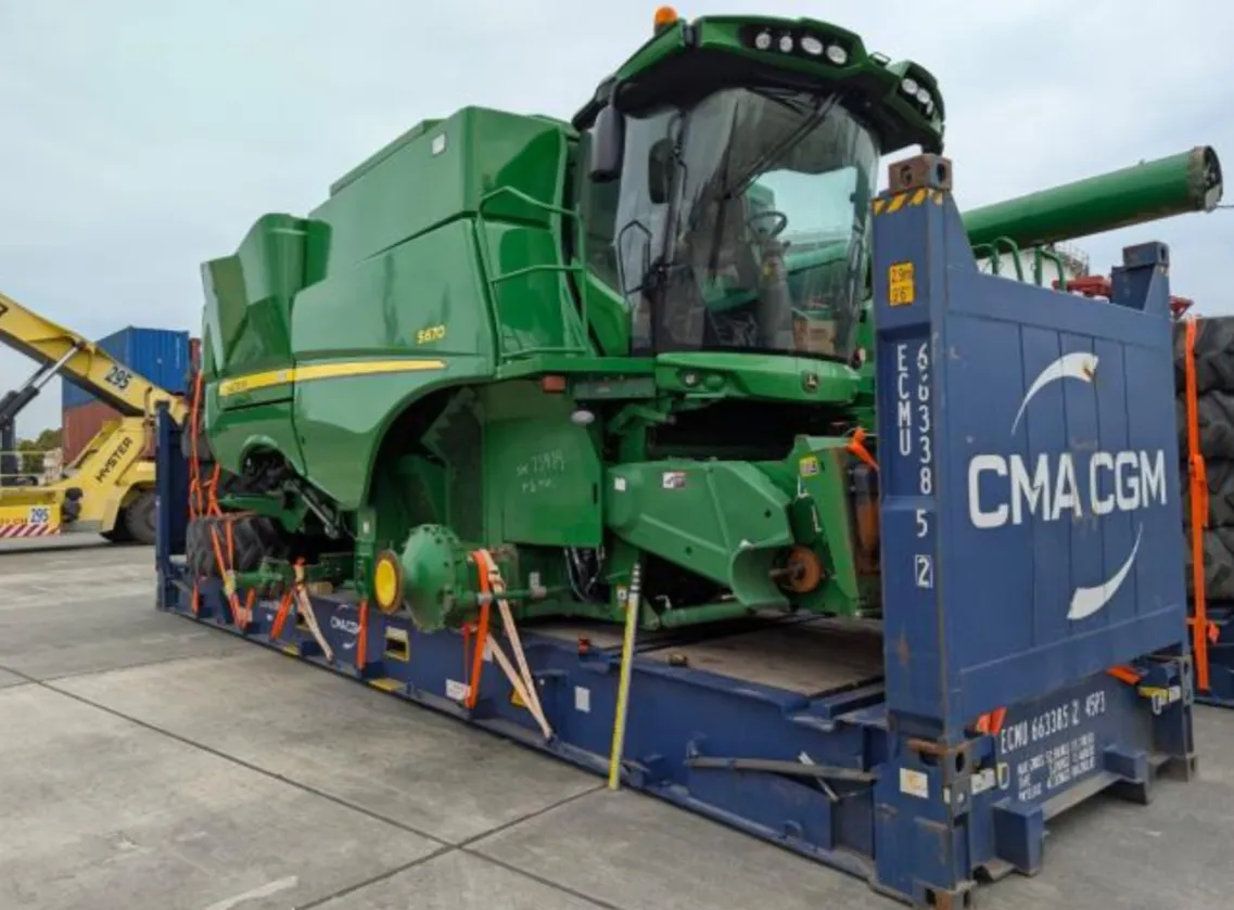 John Deere S670 combine strapped to a flat rack with large wheels stacked beside it