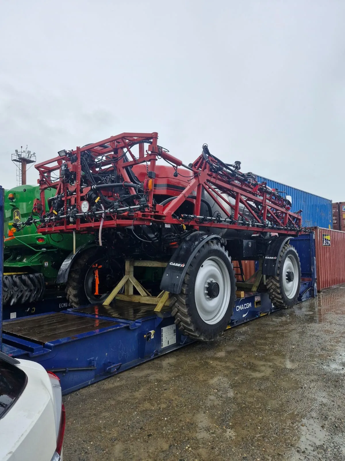 Sprayer standing on a blue platform with a combine beside it and containers behind