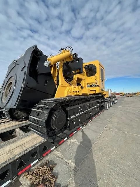 A tracked mining unit with a large cutting wheel on a low trailer in a paved yard