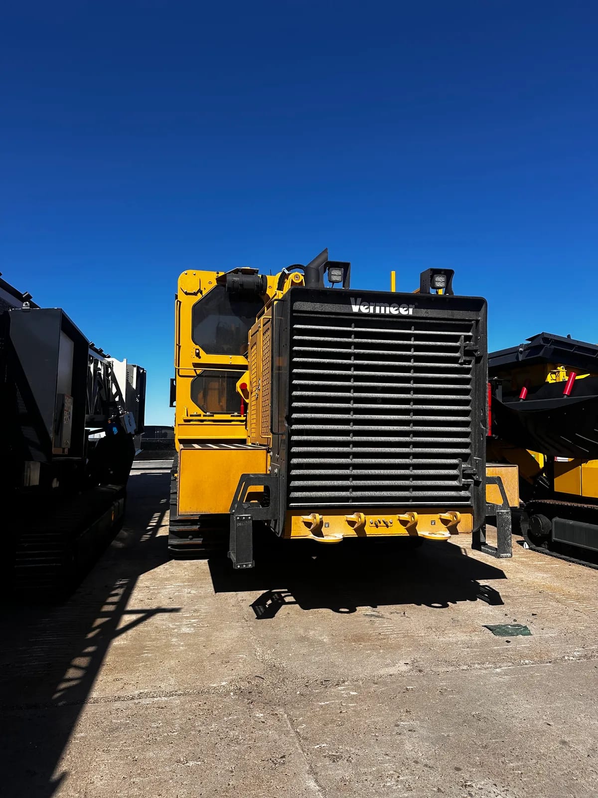 Rear of a yellow tracked Vermeer machine in a paved yard with similar machines on both sides