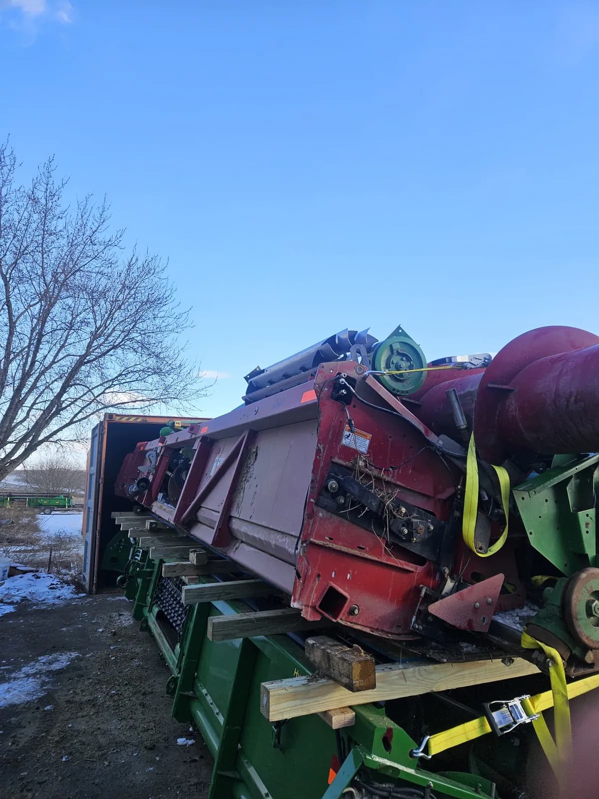 Header resting on timber beams above another header beside an open container, with yellow ratchet straps