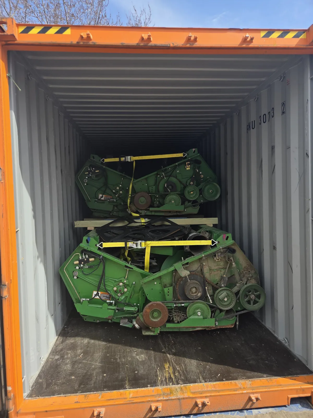 Flex headers stacked on a wooden platform inside a container, secured with yellow straps