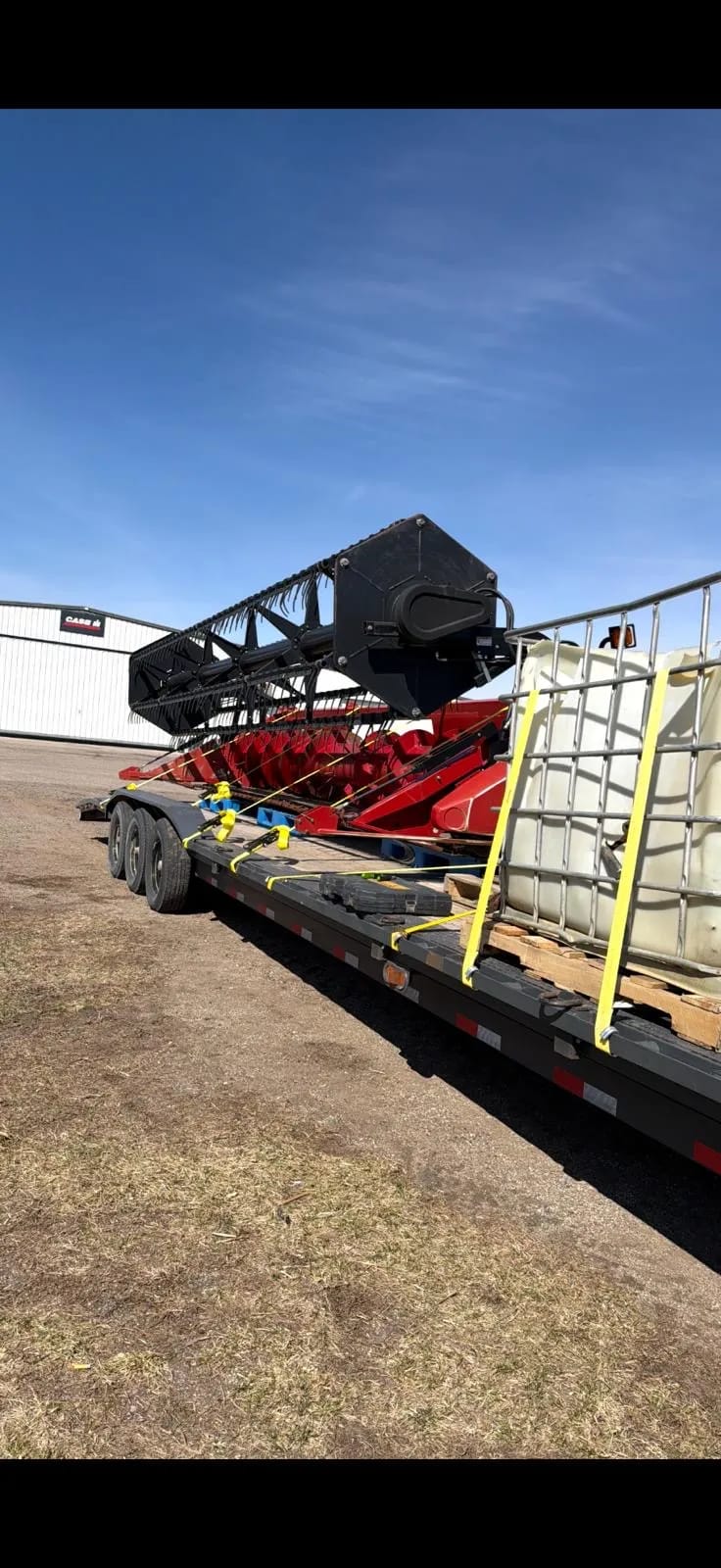 Red header with a black reel strapped to a trailer, with a tank in a metal frame secured beside it