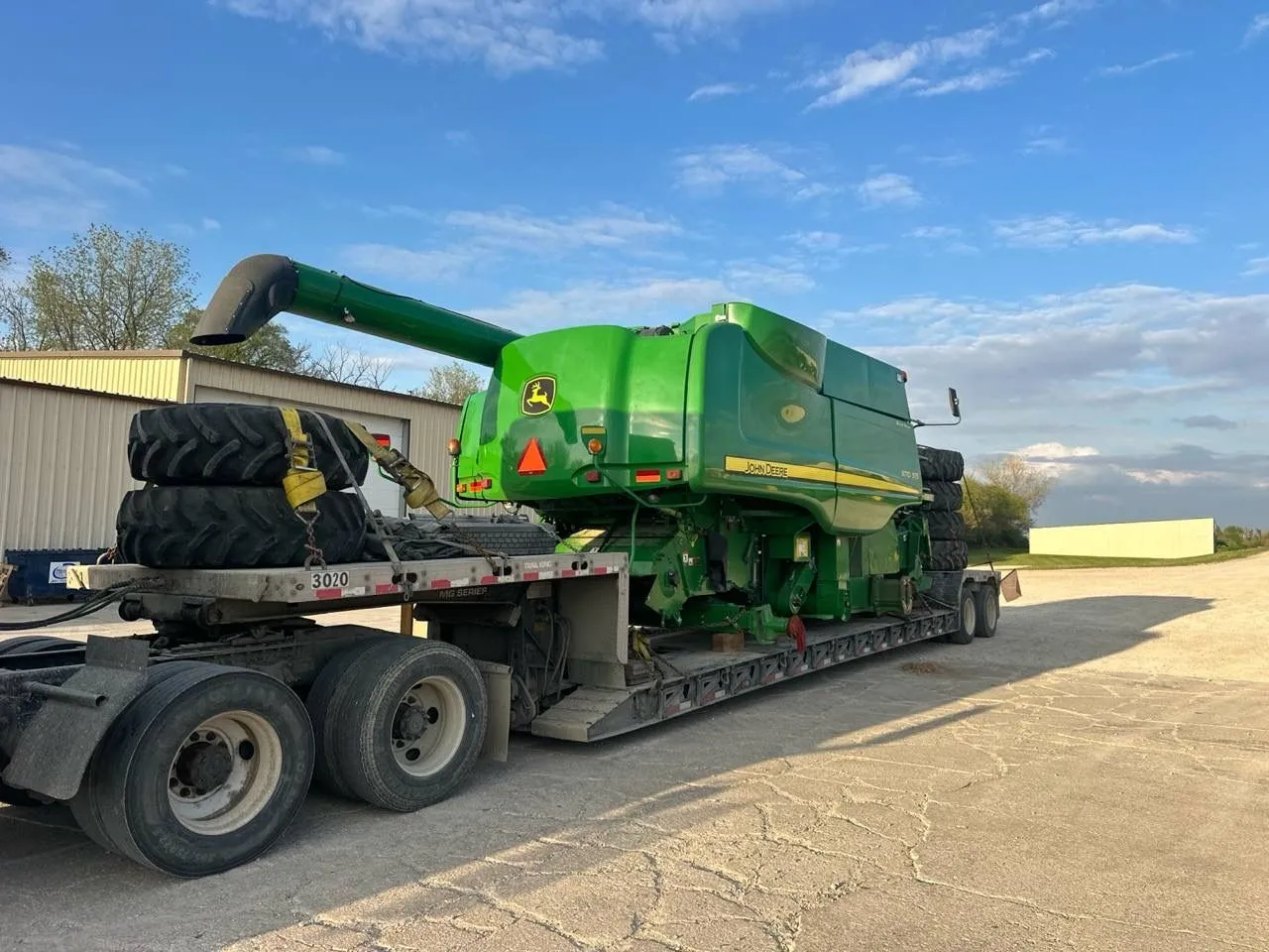 John Deere combine on a low trailer with large wheels stacked and strapped at the front and rear of the deck