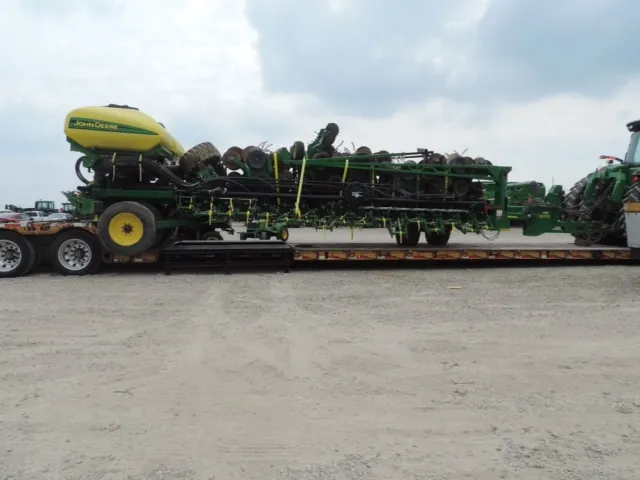 Planter with a yellow seed hopper on a lowboy trailer, part of a green tractor at the right edge
