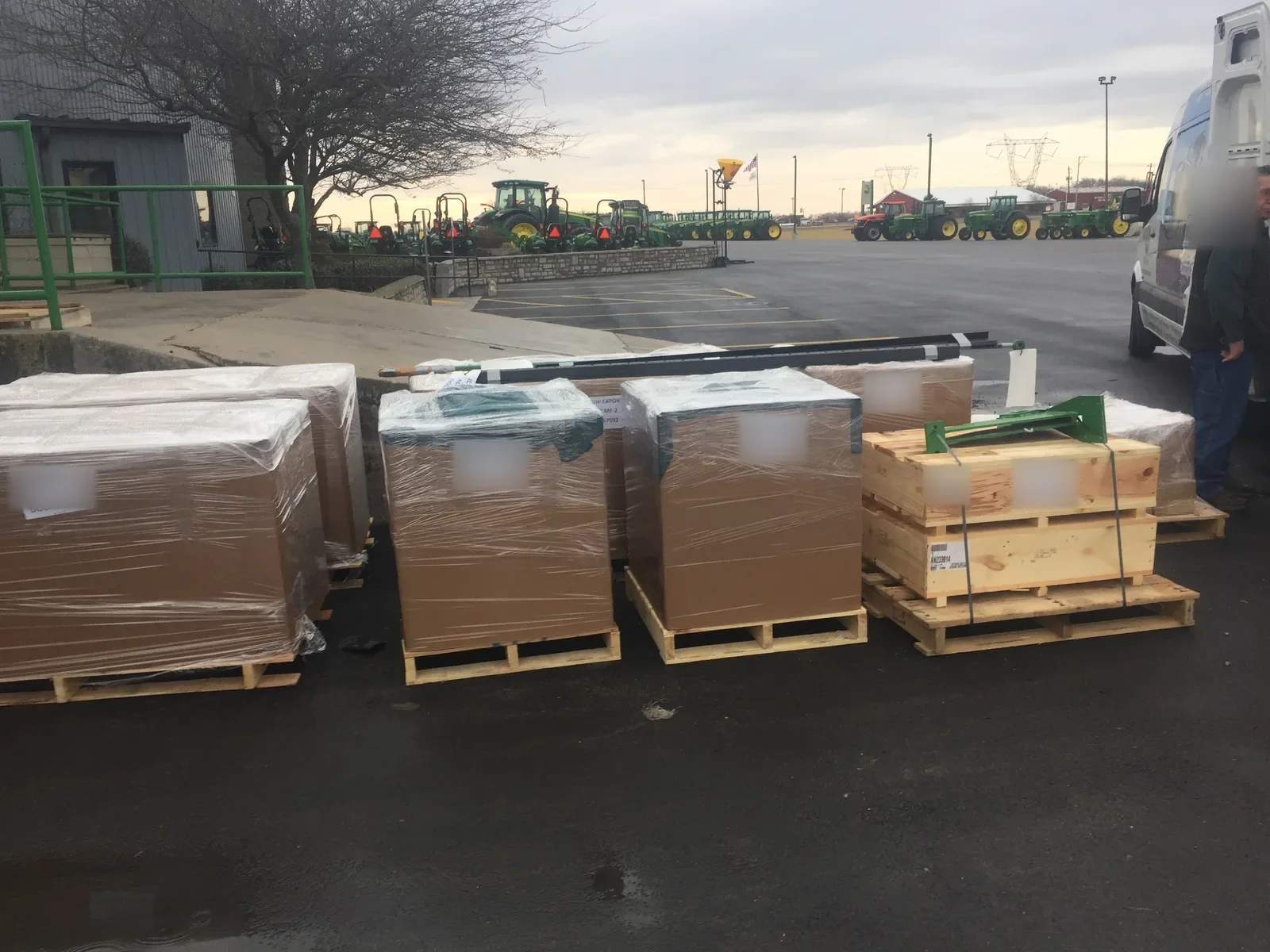 Wrapped boxes and crates on pallets in a car park, with tractors in the distance