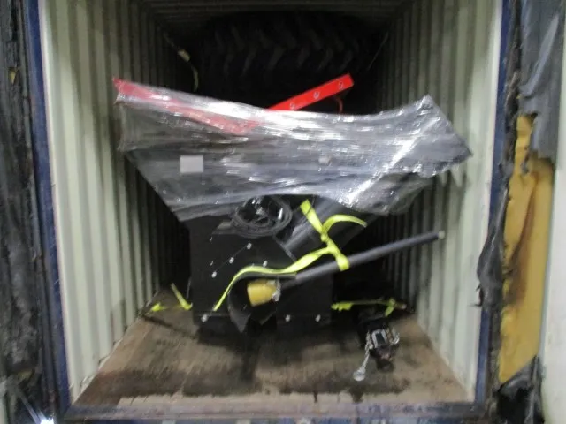 Film-wrapped parts tied down with yellow straps at the rear of a shipping container