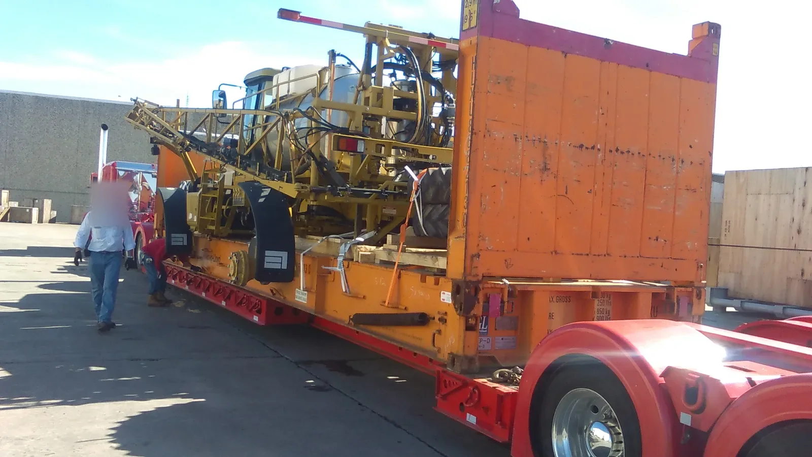 Sprayer on a flat rack beside a tall orange end wall, a worker in a hard hat walking at the left