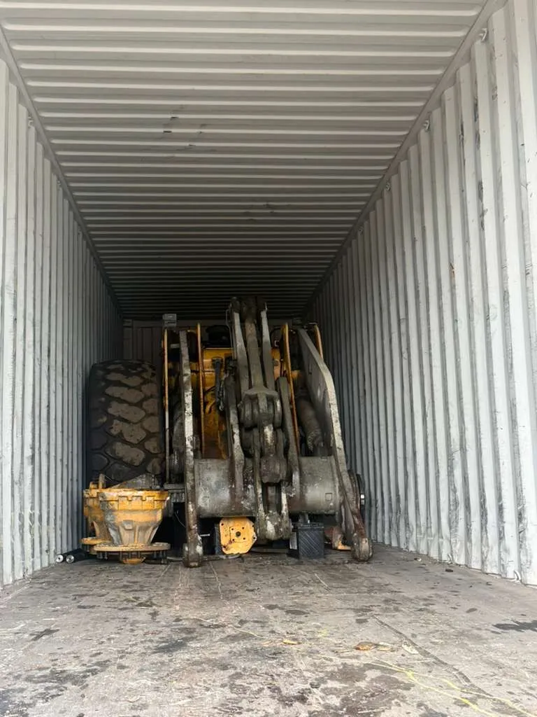 Dismantled loader parts in a container: a large tire, lift arms and yellow hub assemblies