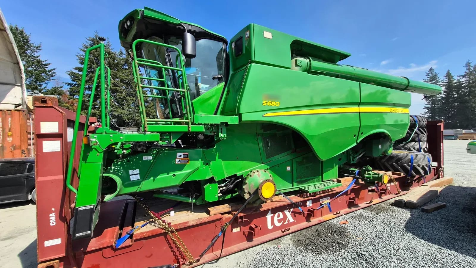 John Deere S680 combine on a Flat Rack seen from the cab side, chained down with tires at the far end