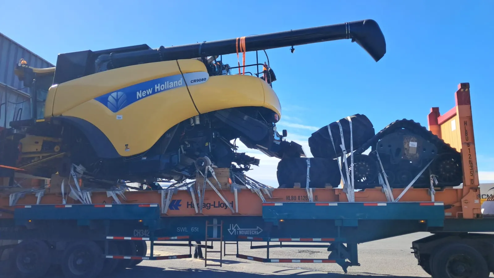New Holland combine strapped down on a Flat Rack with its removed tracks beside it