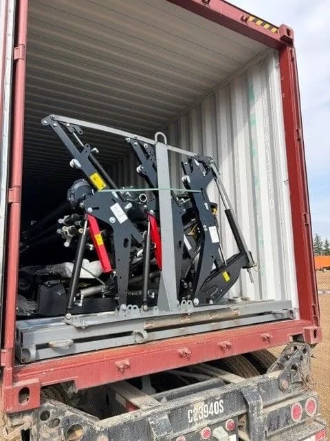 Steel frame with lift arms secured inside a container with open doors, on a trailer