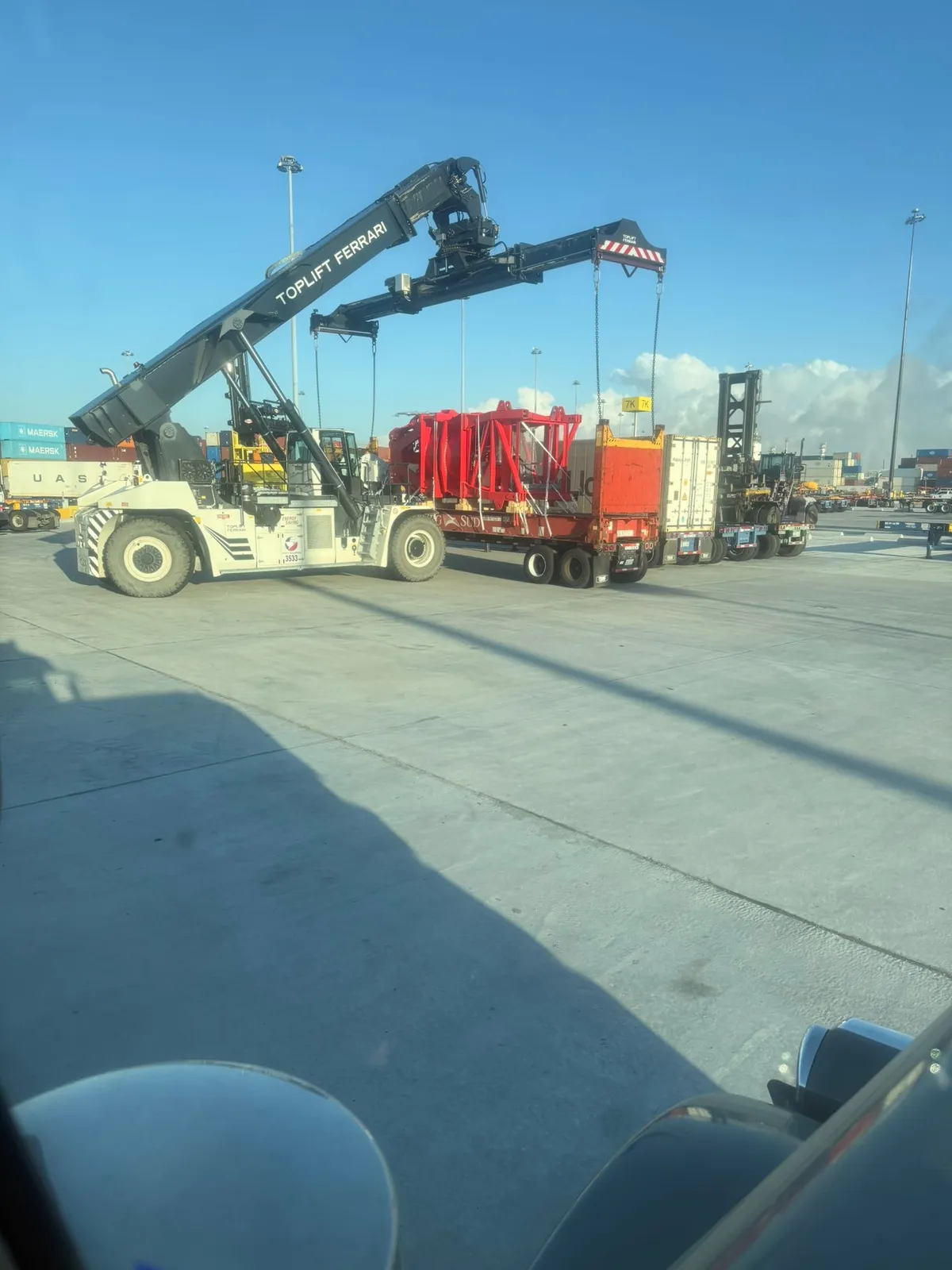 Reach stacker lifting a red load on a flat rack in a port container terminal