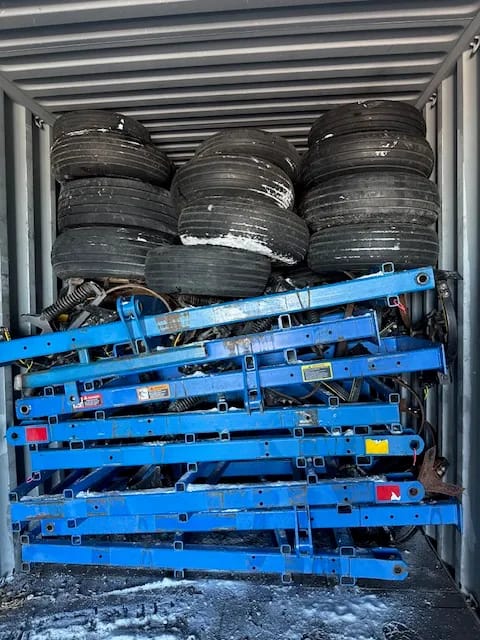Cultivator frame sections in blue and stacked tires loaded inside a container