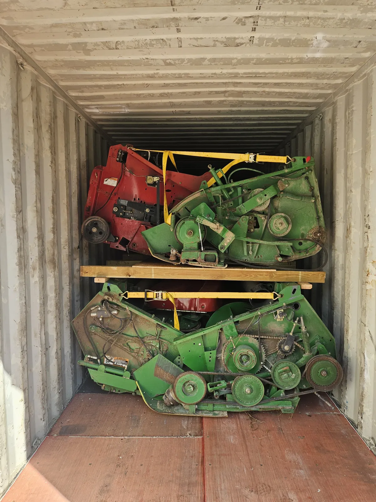 Inside a container: red and green headers on a wooden deck above a green header, held by yellow straps