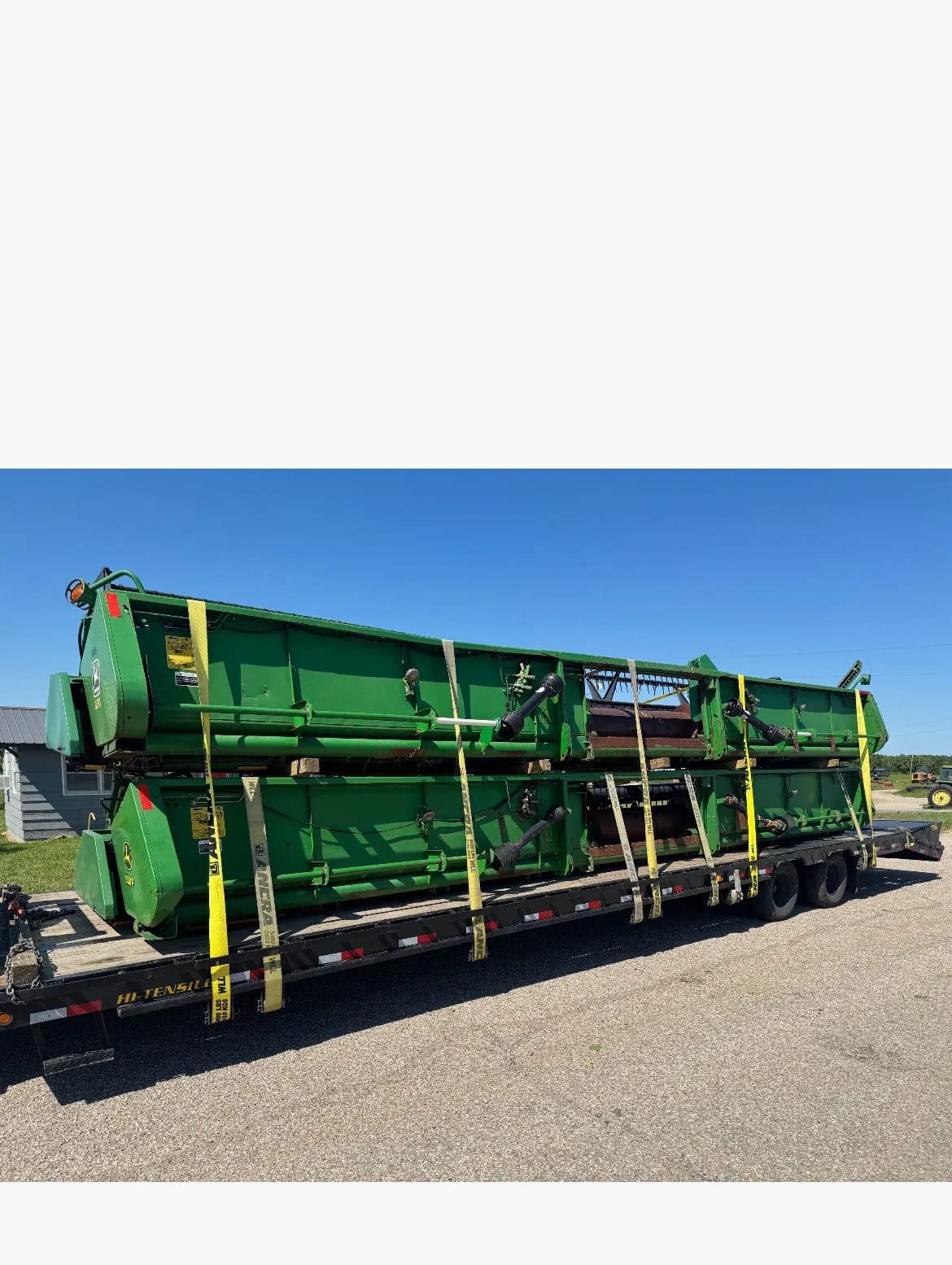 Две жатки John Deere, уложенные друг на друга на платформе трейлера и закреплённые жёлтыми ремнями