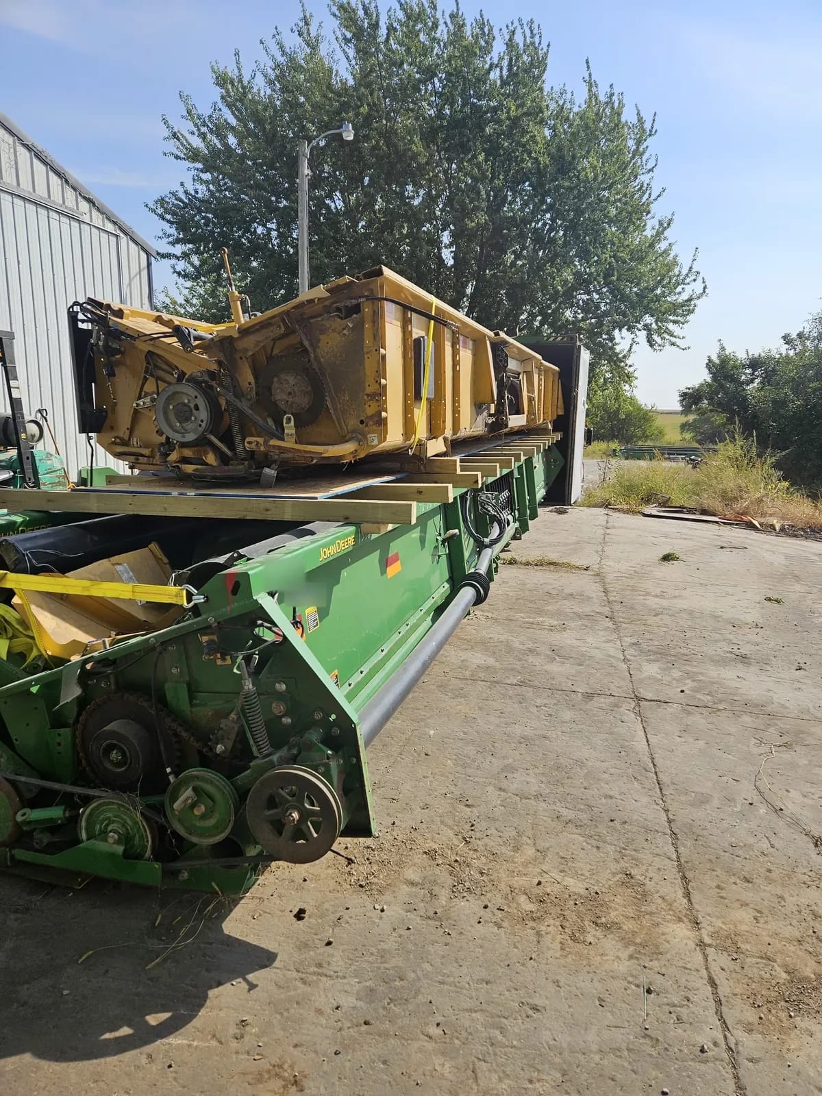 John Deere header on the lower level with a second header resting above it on a wooden deck