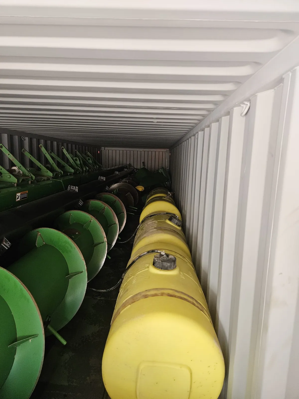 Plastic fertilizer tanks lined along a container wall beside green header parts