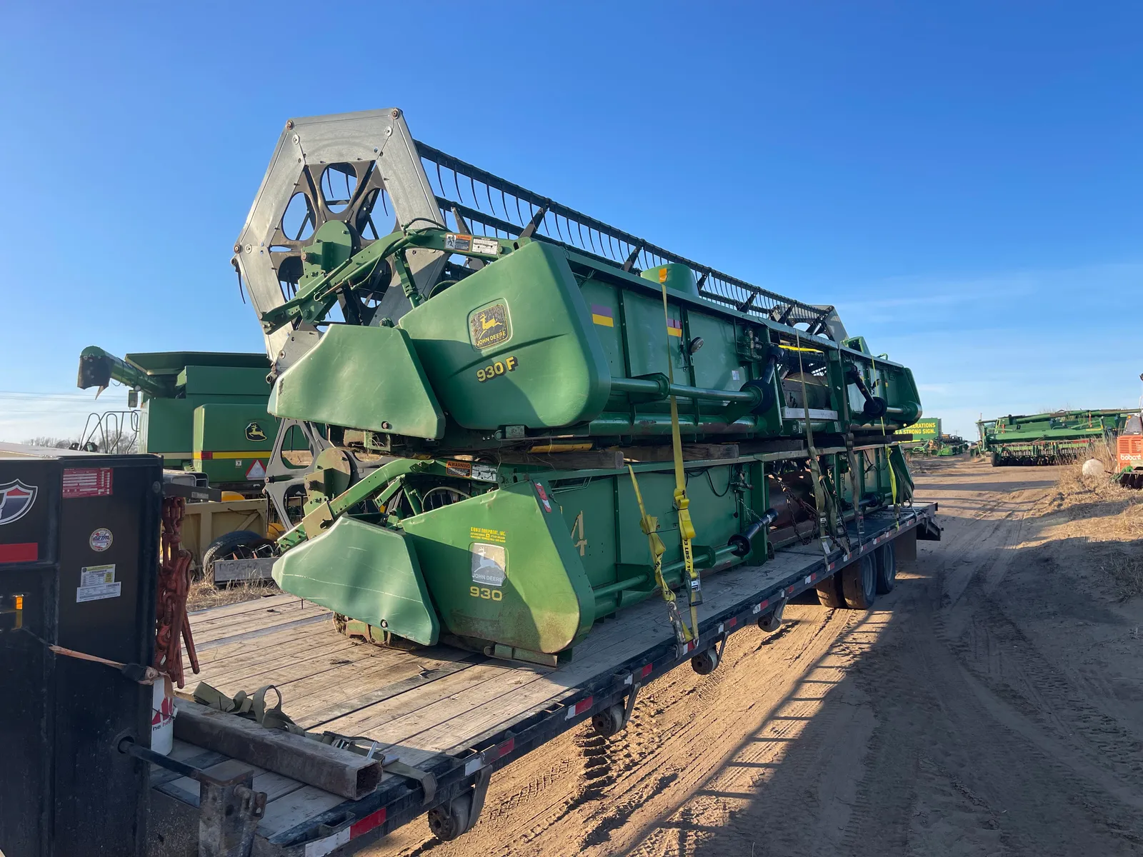 Жатки John Deere 930F, уложенные друг на друга и закреплённые ремнями на платформенном прицепе